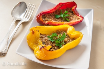 one red and one yellow stuffed, oven baked, peppers, on a rectangular dish with tablespoon and fork on the side
