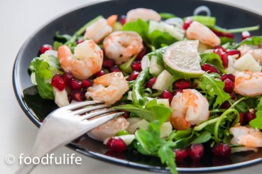 prawn and pomegranate salad with rocket a slice of lime on top, on a black ceramic dish with a fork